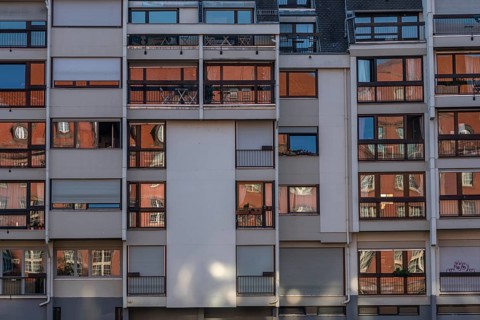 The building has bare facades with numerous balconies. The windows reflect sunlight and create a