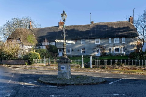 Historic signpost with direction arrows, thatched cottages in village of Pewsey, Wiltshire,