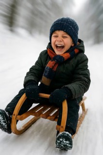 A boy sledges down a hill laughing happily on a sled, symbolizing winter, winter sports, sledding,