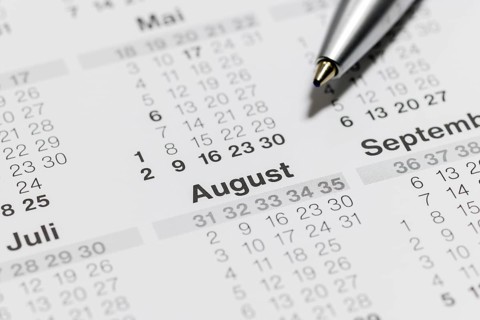 Close-up of a calendar with ballpoint pen pointing to the month of August