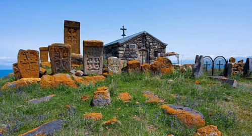 Historic chapel and tombs with stone crosses on a grassy hill, khachkars at the chapel of the Holy