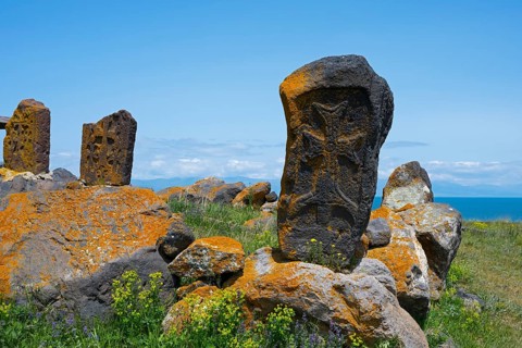 Old tombstones decorated with crosses on a scenic meadow by the sea, khachkars in a cemetery at the