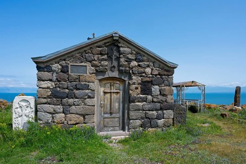 Stone chapel with wooden door in the foreground, sea in the background under clear sky, Chapel of