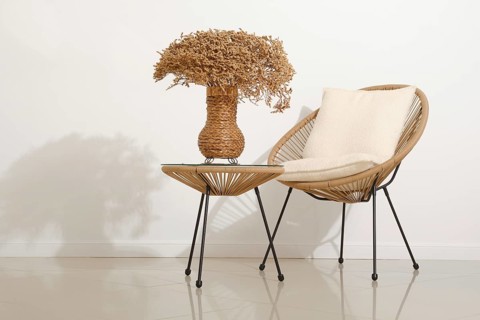 A modern space features a rattan chair with a soft pillow beside a small table. A woven vase filled