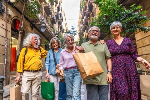 Group of diverse senior friends walking on a narrow city street, holding shopping bags, smiling and