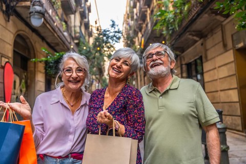 Three smiling senior friends enjoying a day of shopping, holding paper bags while walking in a