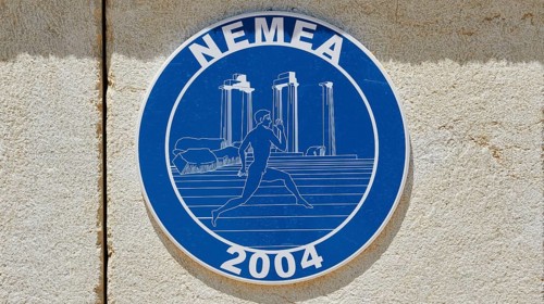 Blue sign with ancient columns and a runner in front of a stone wall, Ancient Stadium, Nemea,