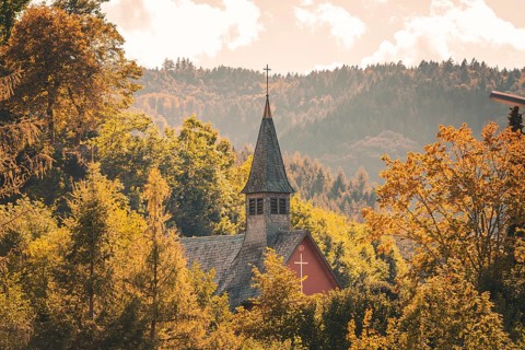 An idyllic church nestled in autumn leaves in front of a mountain landscape