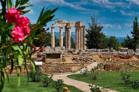 Ancient temple ruins with blooming plants in the foreground under a clear blue sky, Ancient