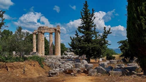 Ruins of an ancient temple against a blue sky with trees and scattered stones, Ancient Zeus