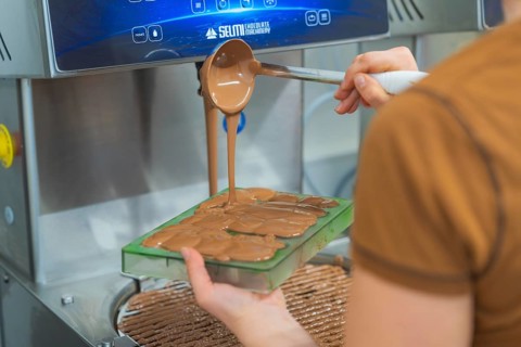 Chocolate is filled into flat molds by a person from a device, Christmas baking, Haselstaller Hof,