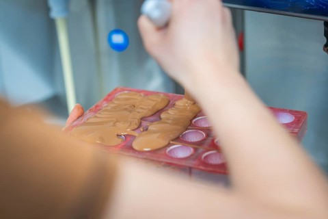 Person fills chocolate into red chocolate molds with a ladle, Christmas baking, Haselstaller Hof,