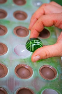 A green, artfully decorated ball is removed from a mold, Weihnachtsbacken, Haselstaller Hof,