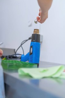 Person uses a blue heat gun to process green objects on a workbench, Weihnachtsbacken, Haselstaller