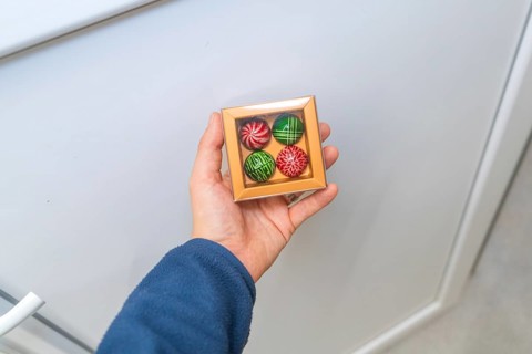 Person holding a chocolate box with patterned chocolates on a light background, Christmas baking,