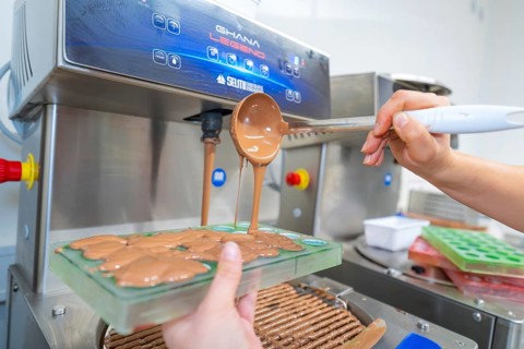 Chocolate filling is poured into molds from a tempering machine, Christmas baking, Haselstaller