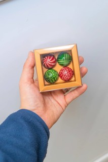 Person holding a box of chocolates with four colorful chocolates, Christmas baking, Haselstaller