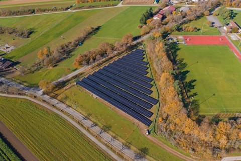 Aerial view of a solar system next to a soccer field in a rural autumn landscape, PV