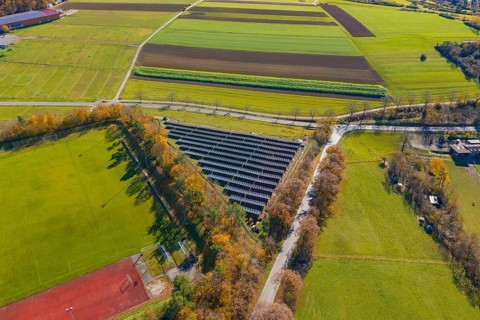 Drone shot of a solar system next to a sports field, surrounded by colorful autumn trees, Bau PV