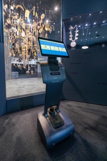 A robot in front of a glass display case full of jewelry in a dark exhibition area, robotic