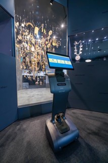 An interactive robot stands in front of an illuminated display case with jewelry in the museum,