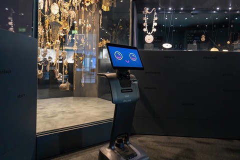 Smiling robot in front of display cabinet with jewelry in museum, robotic personality Roboloutions