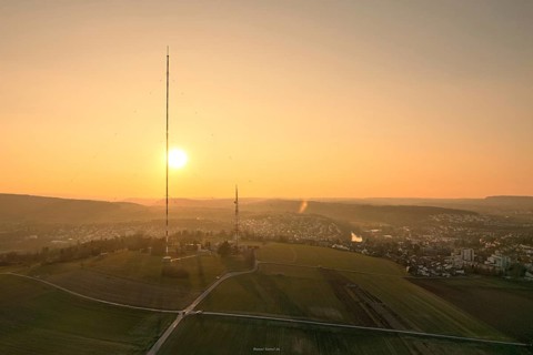 A sunset over countryside and fields with a distinctive transmission tower in the foreground,