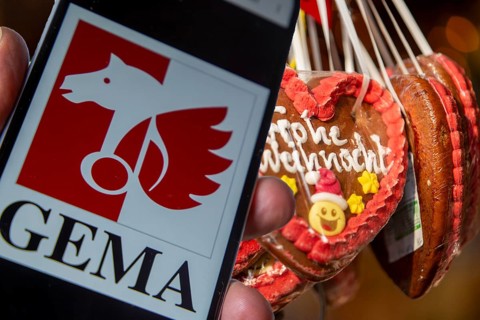 (photo montage) Smartphone with opened GEMA logo in front of a stand at a Christmas market