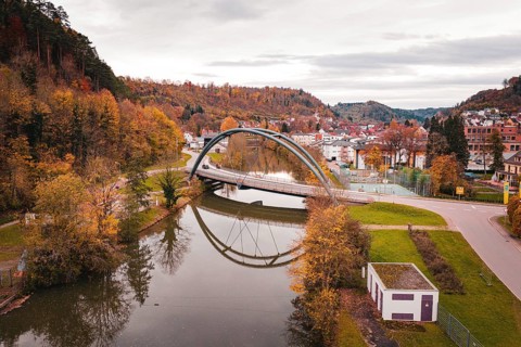 Beautiful bridge in autumn landscape, framed by colorful trees and reflected in water, Sulz am