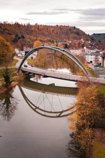 Bridge over a river in an autumn landscape, houses in the background and reflection in the water,
