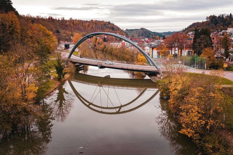 Rustic bridge over a river surrounded by colorful autumn trees and a reflection of the bridge in