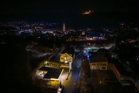 Nighttime view of city with illuminated gas station and distant castle on hill, Nagold, Calw