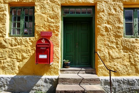Post office, faÃ§ade detail, red mailbox with post horn and crown, green wooden door, yellow wall,