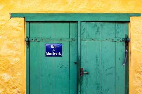 Green wooden door in a yellow wall, blue sign with inscription in Danish language, bathroom and