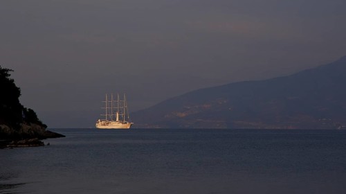 A large sailing ship sails in the calm sea in front of a dark mountain silhouette, Nauplion,