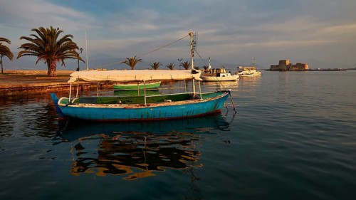 Port of Nauplion, Bourtzi island fortress, A blue boat in the harbor with palm trees and view of a