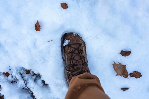 Hiker's brown boot and light pants stepping through fresh white snow scattered with dry brown