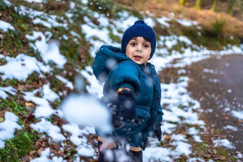 Young boy wearing a blue knitted hat and warm winter jacket, actively playing and throwing a