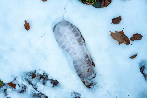 Boot tread leaving a clear imprint in the freshly fallen white snow, surrounded by scattered brown