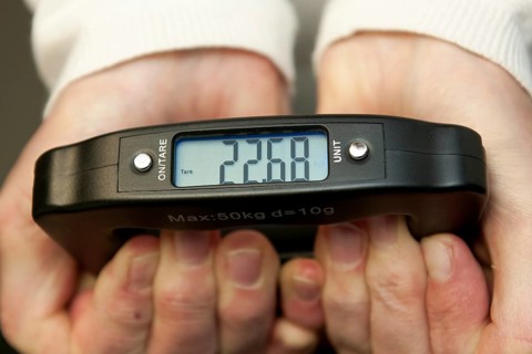Woman holding hand scale for weight of suitcase travel bag flight luggage checks luggage weight for
