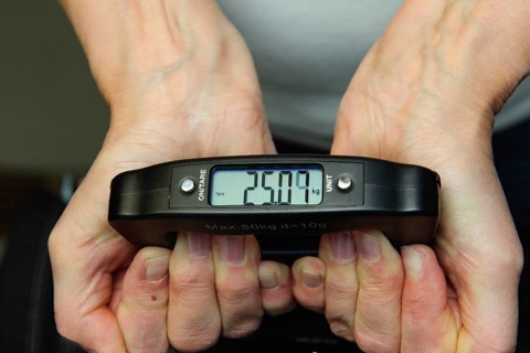 Woman holding hand scale for weight of suitcase travel bag flight luggage checks luggage weight for
