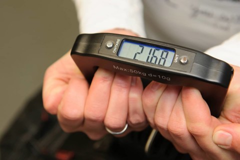 Woman holding hand scale for weight of suitcase travel bag flight luggage checks luggage weight for