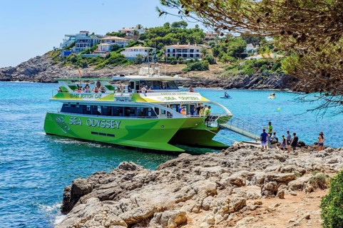 Tourists get on board a glass-bottom boat docks at the small bay Font de Sa Cala on the east coast