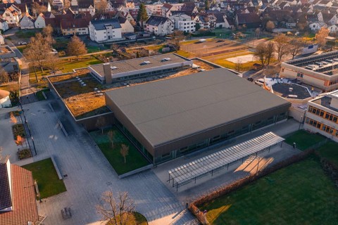 Aerial view of a large, modern building complex with sports facilities and surrounding parking
