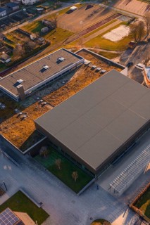 Sports center and swimming pool with flat roof and adjacent parking lot, surrounded by green areas