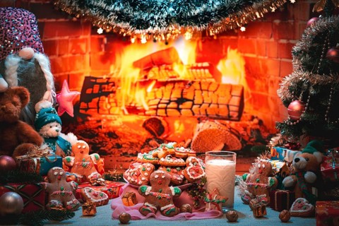 A plate of cookies and a glass of milk next to a Christmas tree and toys in front of a fireplace
