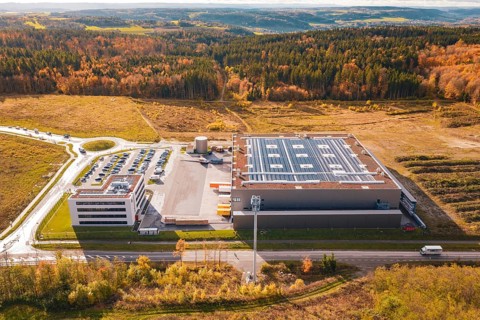Large factory with parking lot, surrounded by forest and open spaces in an autumnal setting, new
