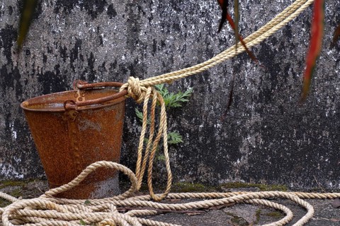 A rusted bucket and rope in front of a weathered well wall, Peermade, Kerala, India