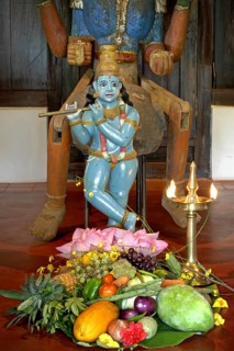 Sculpture of shepherd god Krishna playing his flute, fruits and vegetables lying on the ground,