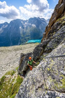 Mountaineer climbs on steep rock face in the secured via ferrata Crocodile Mountain Lake at